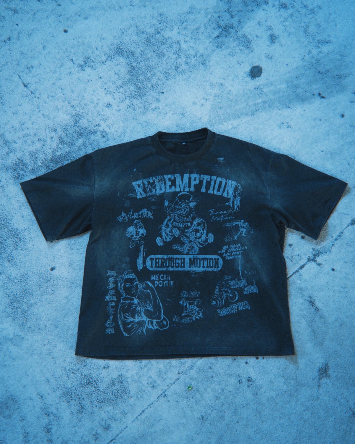 Redemption Through Motion tee, washed black, flat on concrete